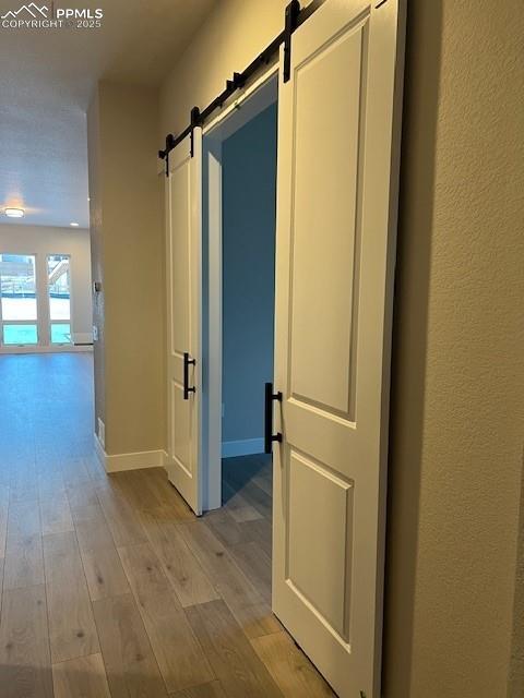 corridor with light wood-type flooring, a barn door, and baseboards