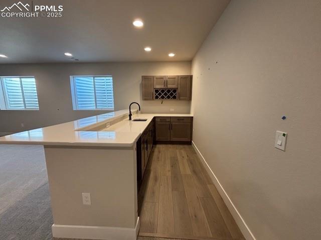 kitchen with light wood finished floors, baseboards, a peninsula, light countertops, and a sink