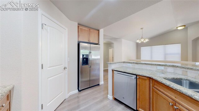 kitchen featuring appliances with stainless steel finishes, light stone counters, pendant lighting, an inviting chandelier, and light hardwood / wood-style flooring