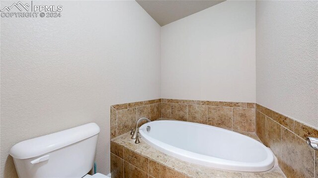 bathroom featuring lofted ceiling, tiled bath, and toilet