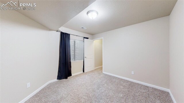 spare room featuring light colored carpet and a textured ceiling