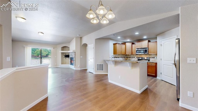 kitchen with appliances with stainless steel finishes, light hardwood / wood-style floors, a kitchen bar, lofted ceiling, and a chandelier