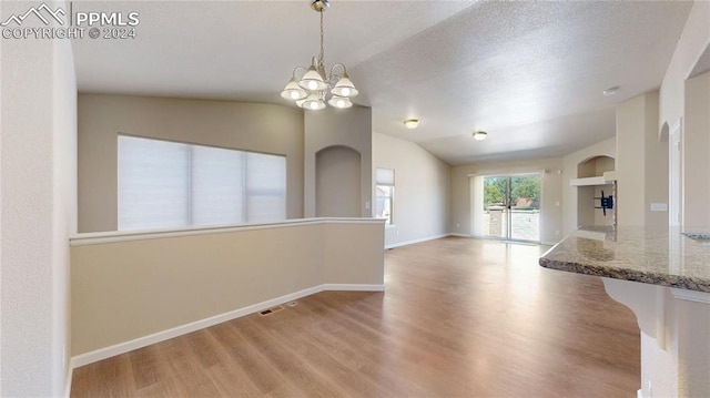 empty room with a notable chandelier, light wood-type flooring, lofted ceiling, and a textured ceiling