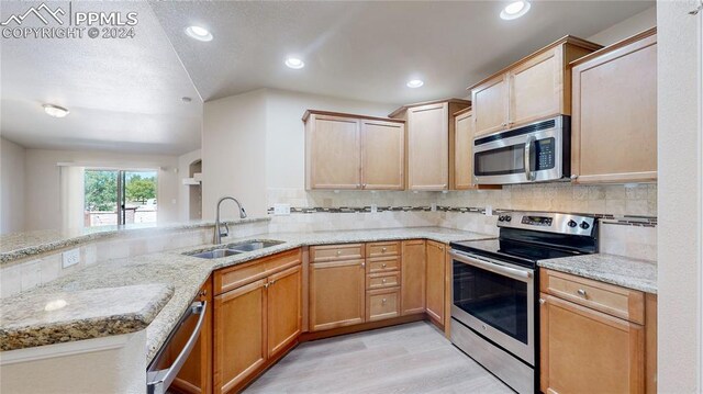 kitchen with appliances with stainless steel finishes, kitchen peninsula, light hardwood / wood-style floors, and sink