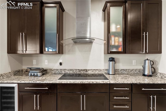 kitchen with light stone counters, wine cooler, dark brown cabinets, wall chimney exhaust hood, and black electric cooktop