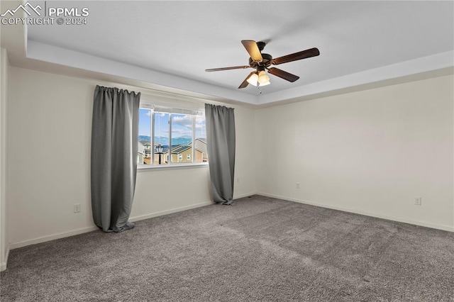 spare room with ceiling fan, a tray ceiling, and carpet flooring