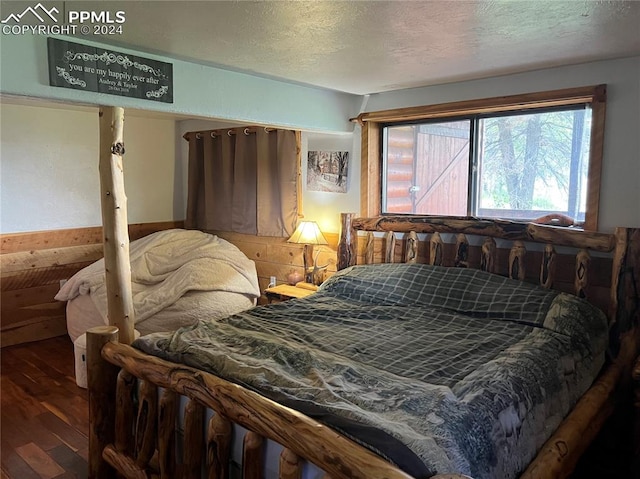 bedroom with a textured ceiling, wood-type flooring, and wooden walls