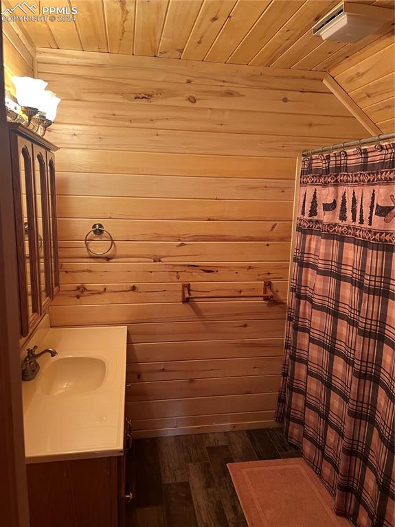 bathroom with wooden walls, wood-type flooring, vanity, and wooden ceiling