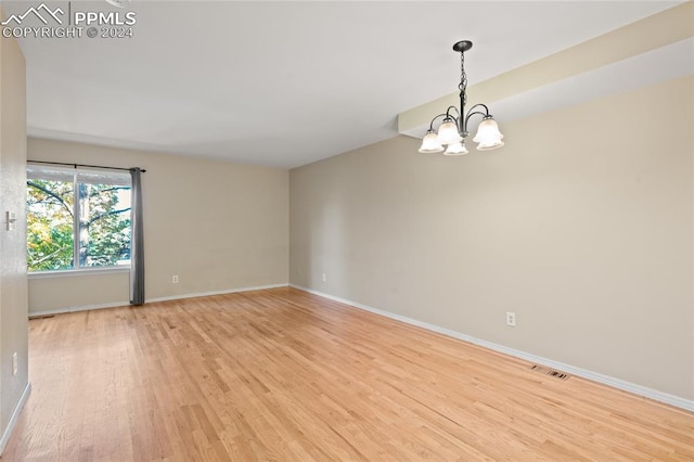 spare room with light wood-type flooring and an inviting chandelier