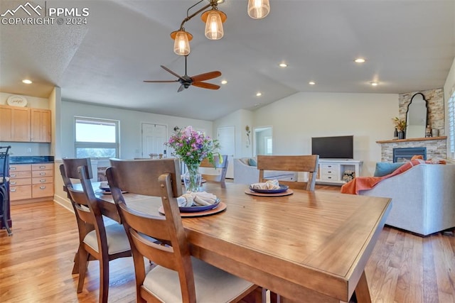 dining space featuring ceiling fan, light wood-type flooring, a fireplace, and lofted ceiling