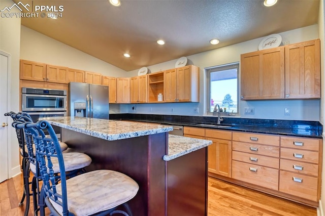 kitchen featuring sink, a kitchen island, appliances with stainless steel finishes, light stone countertops, and vaulted ceiling