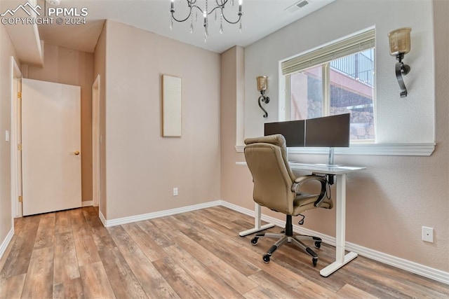 office with light wood-type flooring and an inviting chandelier