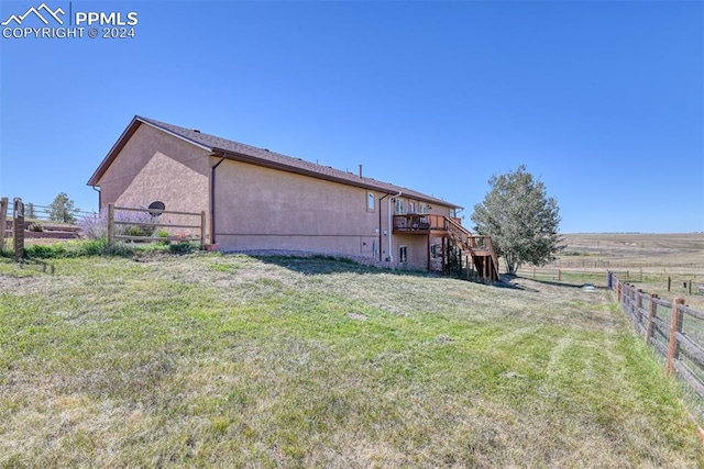 rear view of house featuring a rural view, a deck, and a lawn