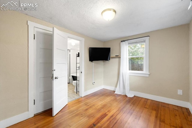 unfurnished bedroom with ensuite bath, a textured ceiling, and hardwood / wood-style floors