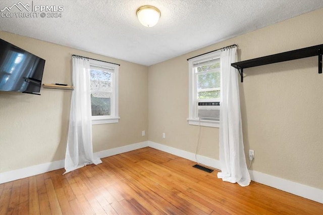 spare room with cooling unit, a textured ceiling, plenty of natural light, and hardwood / wood-style floors