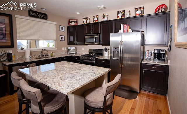 6777 Ironwood Tree Cir, Colorado Springs, CO 80927 - kitchen with a kitchen breakfast bar, light stone countertops, a sink, light wood finished floors, and stainless steel appliances