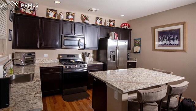 6777 Ironwood Tree Cir, Colorado Springs, CO 80927 - kitchen featuring light stone countertops, appliances with stainless steel finishes, a breakfast bar, a sink, and light wood-style floors