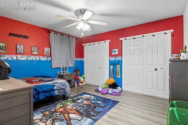 bedroom with a textured ceiling, two closets, ceiling fan, and light hardwood / wood-style flooring