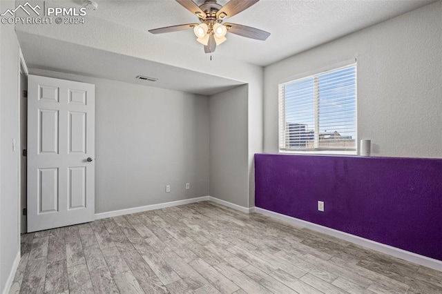 empty room with a textured ceiling, ceiling fan, and light hardwood / wood-style flooring