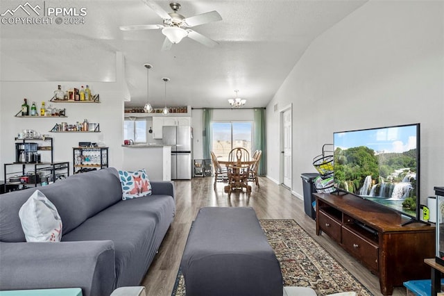 living room with ceiling fan with notable chandelier, a textured ceiling, lofted ceiling, and hardwood / wood-style floors