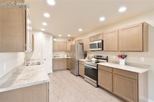 kitchen with sink, light hardwood / wood-style flooring, appliances with stainless steel finishes, light brown cabinetry, and light stone countertops