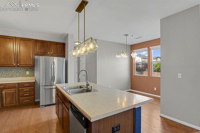 kitchen featuring appliances with stainless steel finishes, light wood-type flooring, sink, and an island with sink