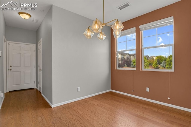 empty room featuring an inviting chandelier and hardwood / wood-style flooring