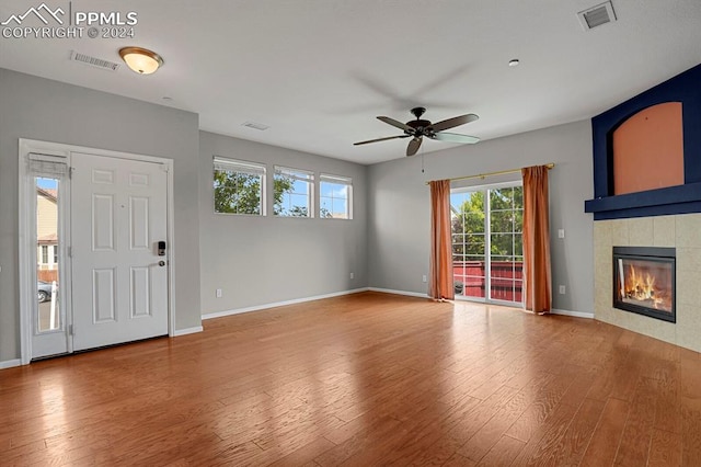 unfurnished living room featuring ceiling fan, hardwood / wood-style flooring, a tile fireplace, and a wealth of natural light