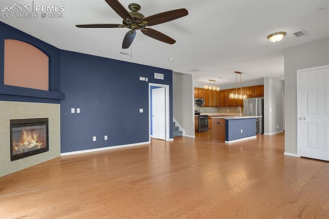 unfurnished living room with ceiling fan with notable chandelier, sink, a fireplace, and light hardwood / wood-style floors