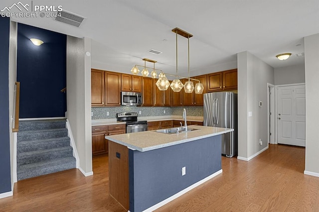 kitchen with sink, tasteful backsplash, a center island with sink, stainless steel appliances, and light wood-type flooring