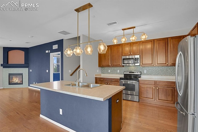 kitchen featuring an island with sink, hanging light fixtures, sink, appliances with stainless steel finishes, and light wood-type flooring