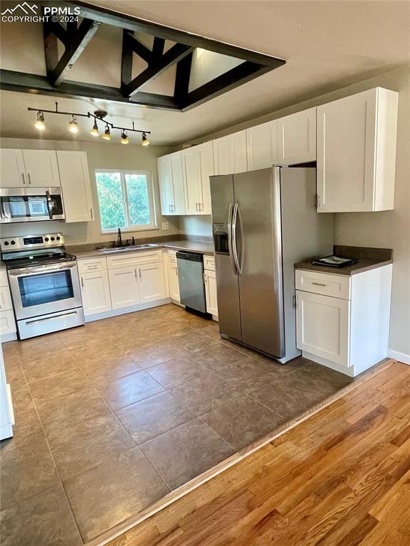 kitchen featuring white cabinets, sink, light hardwood / wood-style flooring, stainless steel appliances, and lofted ceiling with beams