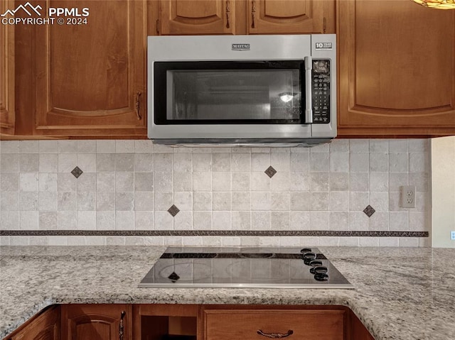 kitchen with light stone countertops, backsplash, and black electric cooktop