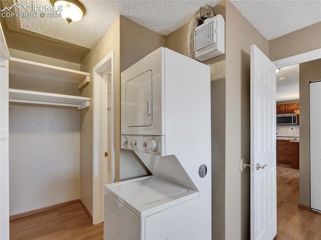 laundry area with a textured ceiling, stacked washing maching and dryer, and light hardwood / wood-style flooring