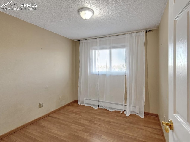 empty room featuring a textured ceiling, light hardwood / wood-style flooring, and a baseboard radiator