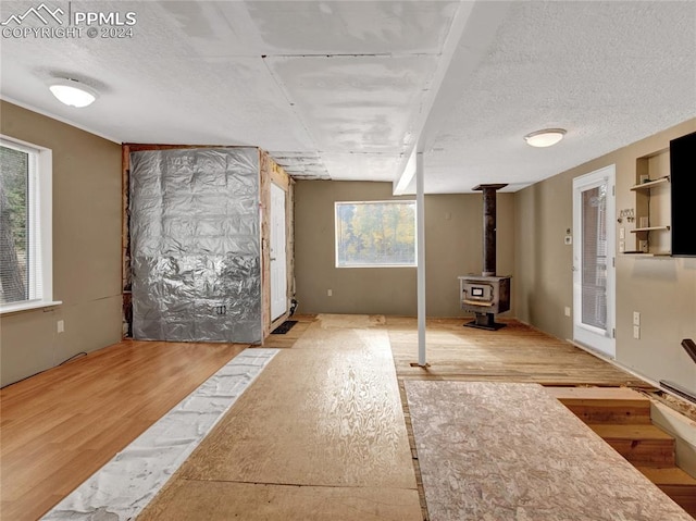 basement featuring a textured ceiling, light hardwood / wood-style flooring, and a wood stove