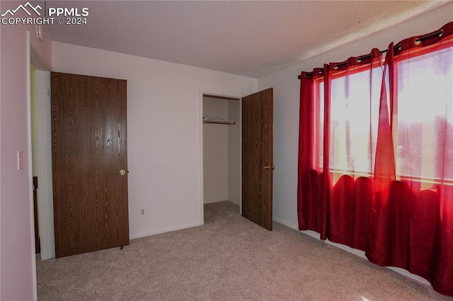 unfurnished bedroom with light colored carpet, a textured ceiling, and a closet