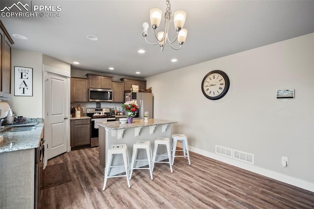 kitchen featuring a notable chandelier, light stone countertops, stainless steel appliances, and hardwood / wood-style flooring