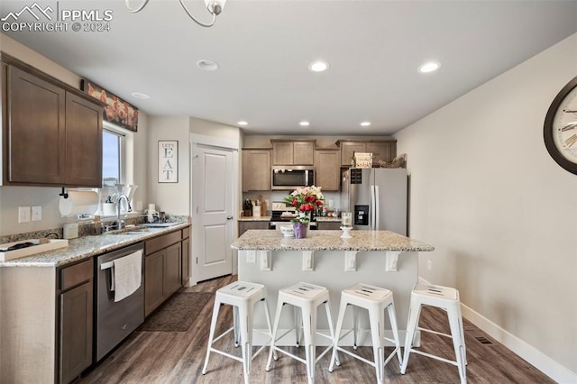 kitchen with sink, a kitchen island, stainless steel appliances, light stone countertops, and dark hardwood / wood-style flooring