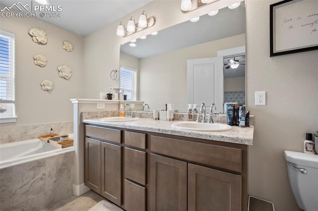 bathroom featuring ceiling fan, tiled bath, vanity, and toilet