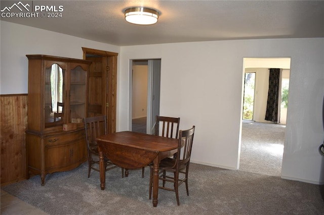 carpeted dining area featuring wooden walls