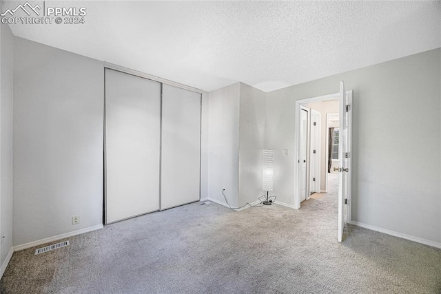 unfurnished bedroom featuring a textured ceiling, light carpet, and a closet