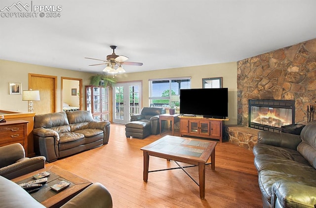 living room featuring ceiling fan, a stone fireplace, and light wood-type flooring