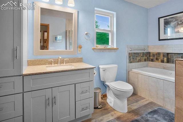 bathroom featuring hardwood / wood-style floors, tiled bath, vanity, and toilet