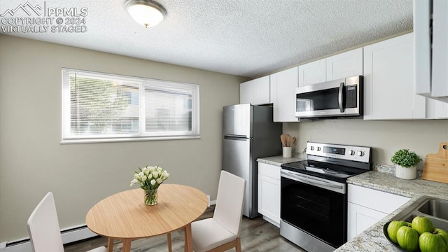 kitchen featuring light stone counters, white cabinets, appliances with stainless steel finishes, and light hardwood / wood-style floors