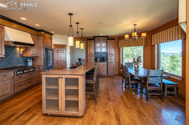 kitchen featuring a kitchen island with sink, hardwood / wood-style flooring, appliances with stainless steel finishes, custom range hood, and a breakfast bar area