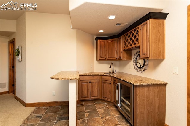 kitchen featuring light stone countertops, wine cooler, dark carpet, and sink