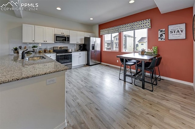 kitchen with light stone countertops, stainless steel appliances, white cabinets, and sink