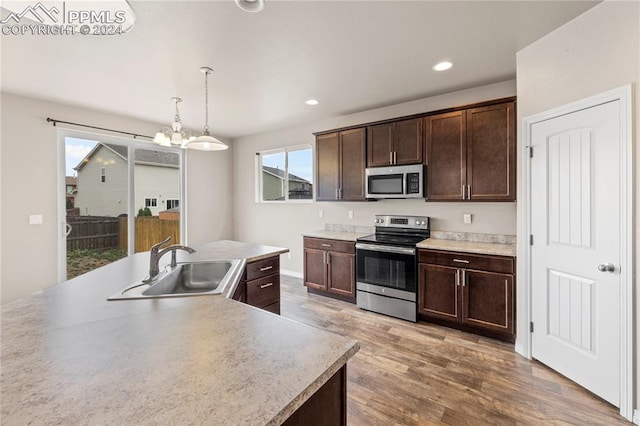 kitchen with pendant lighting, light hardwood / wood-style floors, a kitchen island with sink, sink, and stainless steel appliances