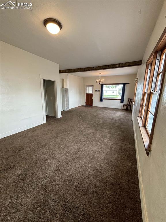 unfurnished living room featuring dark carpet and a chandelier